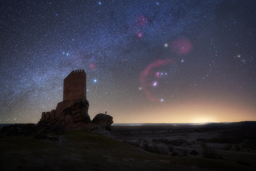 Cielo nocturno estrellado con la constelación de Orion y nebulosas y el castillo de Zafra en el primer plano