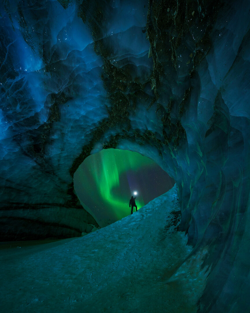 Bright Aurora seen from the opening of an ice cave with a person standing outside the cave