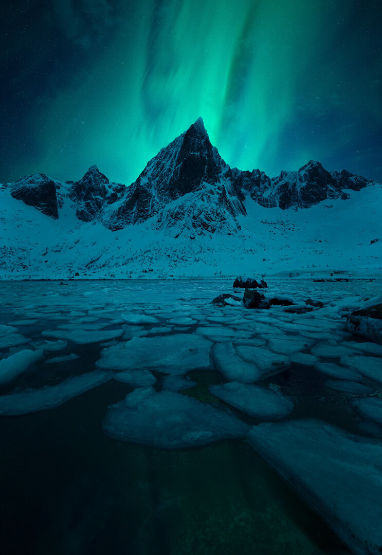Aurora Borealis covering the sky over several mountain peaks and a frozen lake