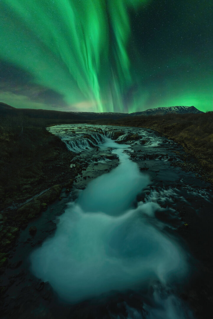 Una Aurora brilla fuerte en el cielo nocturno sobre Brúarfoss
