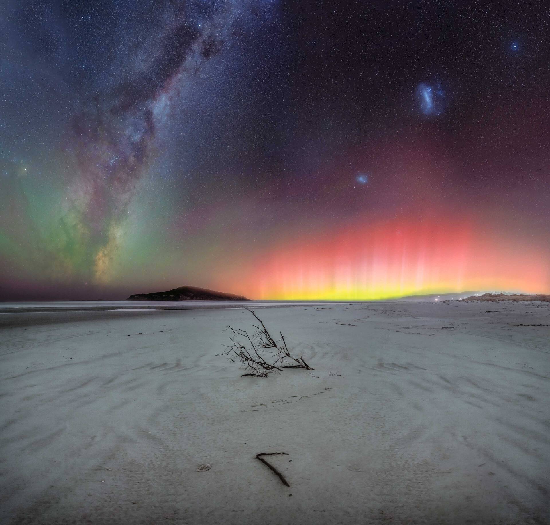 Milky Way core dominating the night sky alongside the Magellanic Clouds and a bright red Aurora