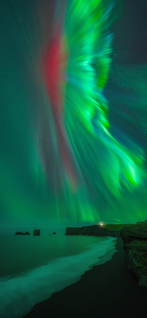 Panorámica vertical que muestra una Aurora de color rojo y verde cubriendo el cielo sobre una playa