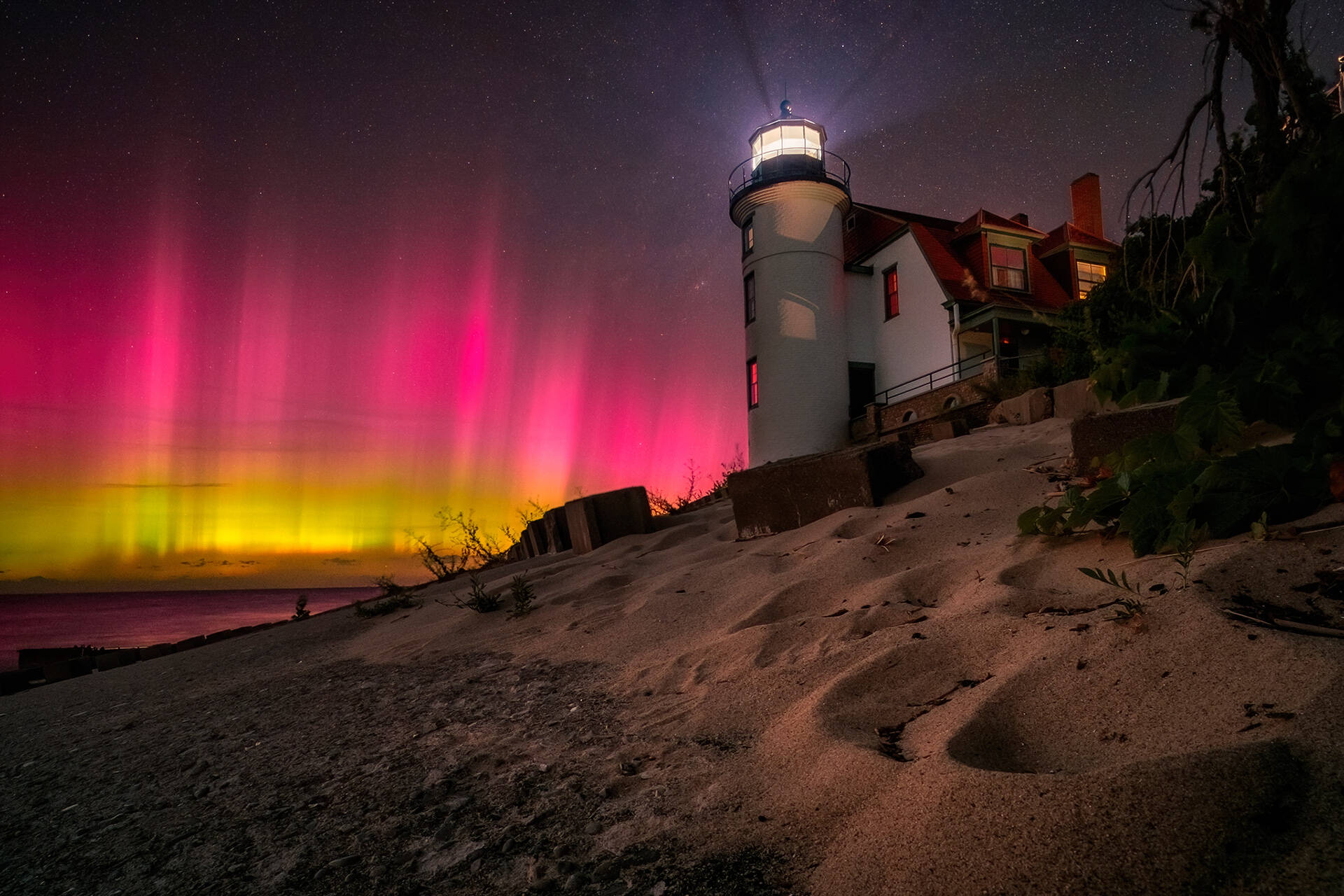 Foto da Aurora boreal vermelha brilhante cobrindo o céu noturno com um farol em Michigan EUA