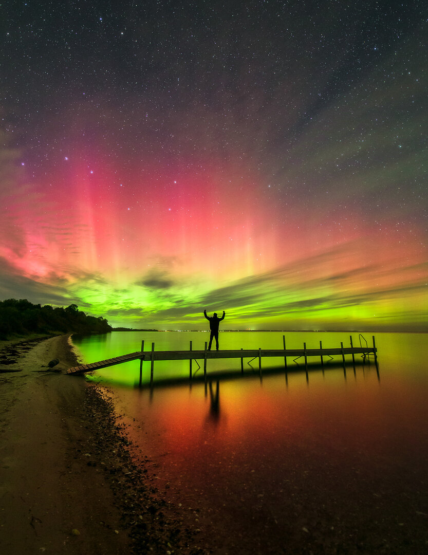Aurora de color rojo intenso cube el cielo nocturna y refleja su luz sobre un lago