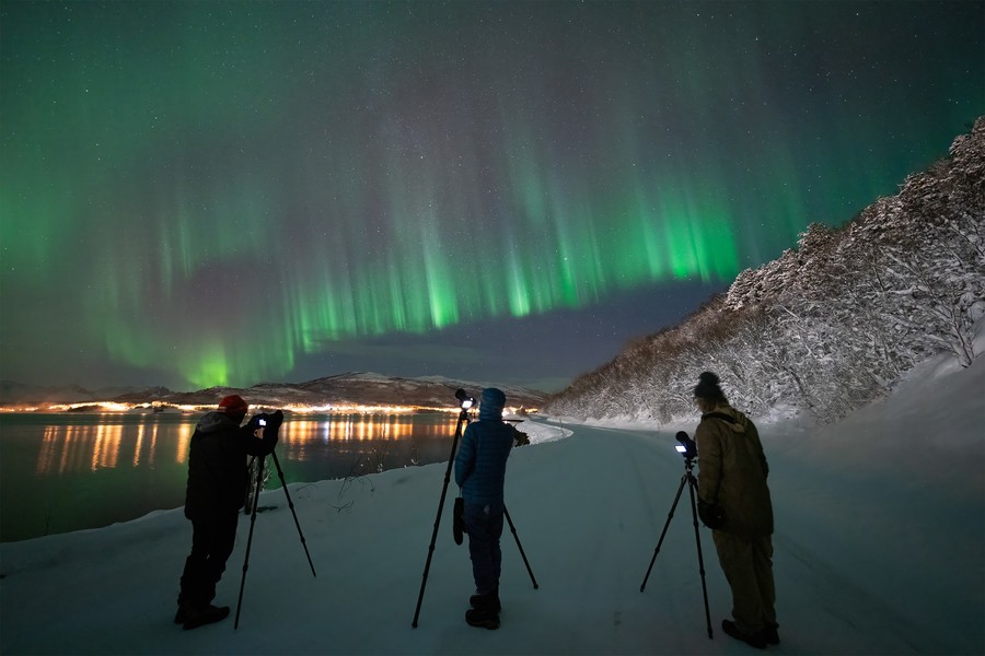 Best hours to see Northern Lights Three photographers taking a photo of the Northern Lights in Norway